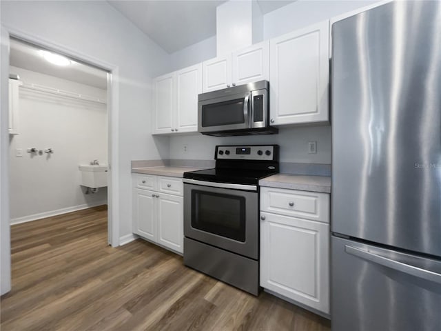 kitchen featuring lofted ceiling, stainless steel appliances, dark wood-type flooring, and white cabinetry