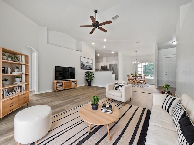 living room featuring ceiling fan with notable chandelier, lofted ceiling, and light hardwood / wood-style flooring