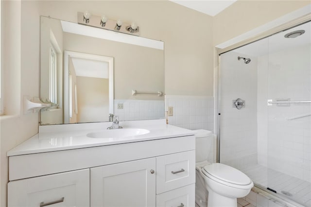 full bathroom with vanity, a wainscoted wall, a stall shower, tile walls, and toilet