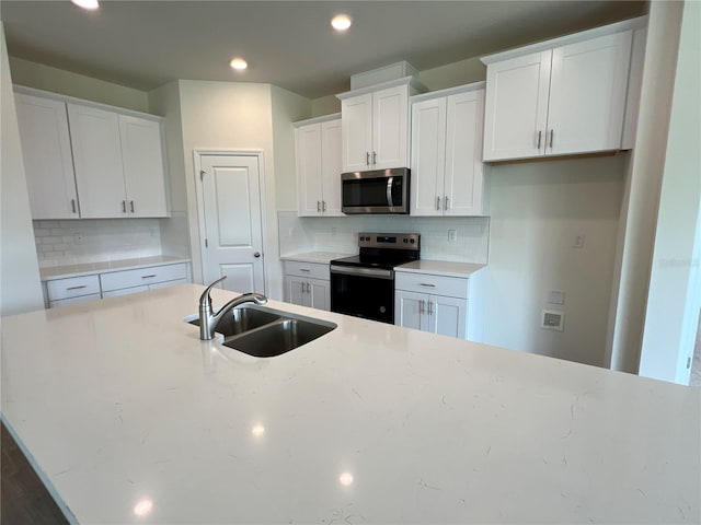 kitchen featuring sink, appliances with stainless steel finishes, white cabinetry, backsplash, and light stone countertops