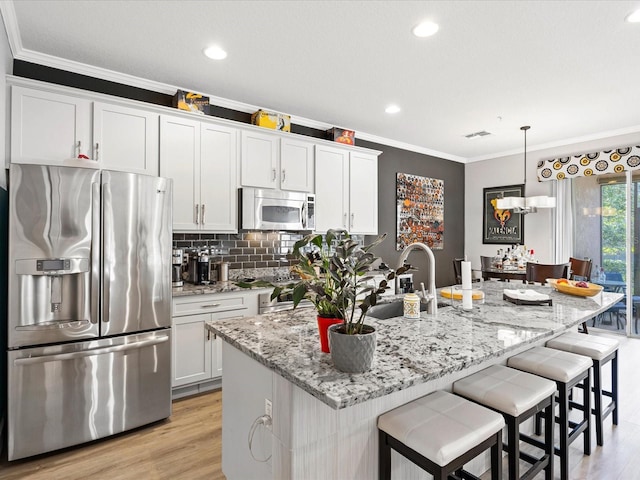 kitchen featuring white cabinetry, stainless steel appliances, an island with sink, and light stone counters