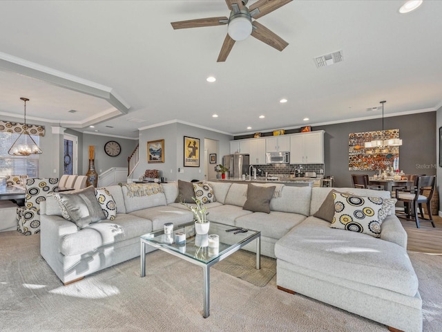 living room featuring ceiling fan with notable chandelier, ornamental molding, and light colored carpet