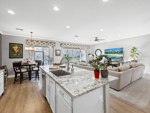 kitchen with an island with sink, light stone countertops, sink, and white cabinets