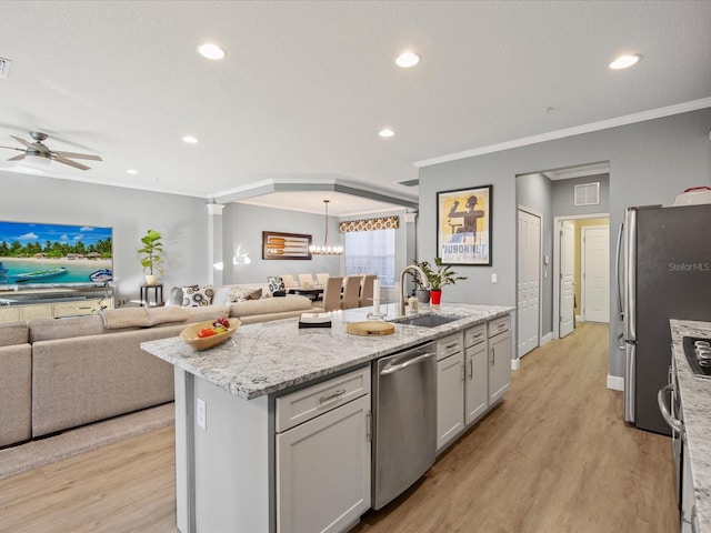 kitchen featuring sink, stainless steel appliances, ornamental molding, light hardwood / wood-style floors, and a center island with sink