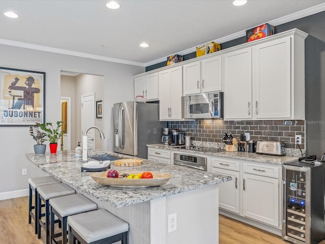 kitchen featuring wine cooler, white cabinetry, appliances with stainless steel finishes, and a kitchen island with sink