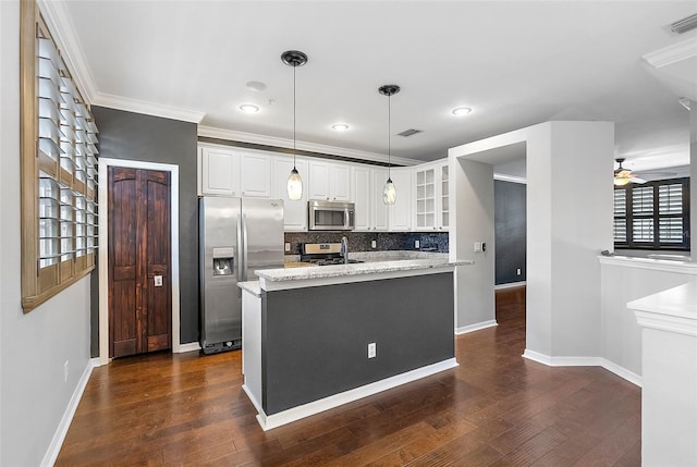 kitchen featuring appliances with stainless steel finishes, decorative light fixtures, white cabinets, a kitchen island with sink, and light stone counters