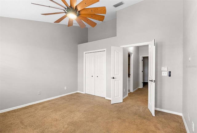 unfurnished bedroom with ceiling fan, a closet, carpet, and a high ceiling