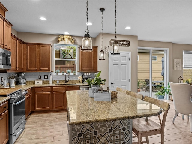 kitchen with sink, stainless steel appliances, a center island, light stone counters, and hanging light fixtures