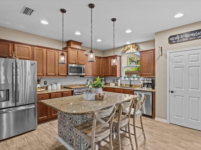 kitchen featuring light stone counters, hanging light fixtures, stainless steel appliances, a kitchen island, and a breakfast bar area