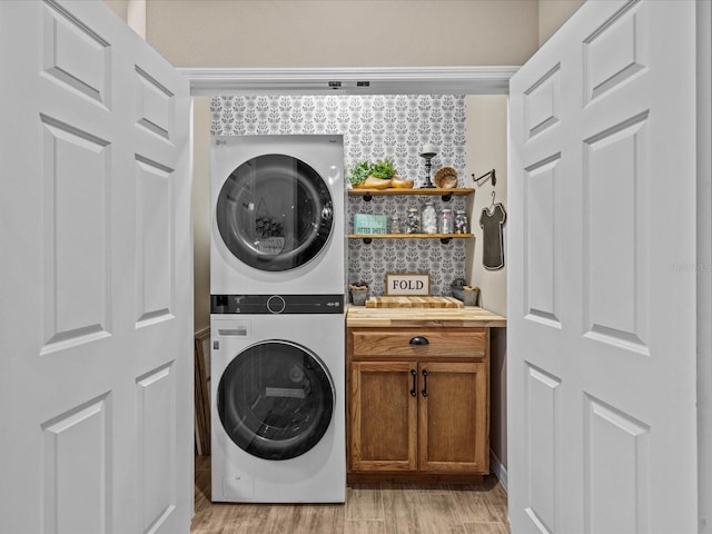 clothes washing area with stacked washer and clothes dryer, cabinets, and light hardwood / wood-style flooring