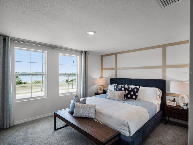 bedroom featuring a textured ceiling, a water view, and carpet flooring