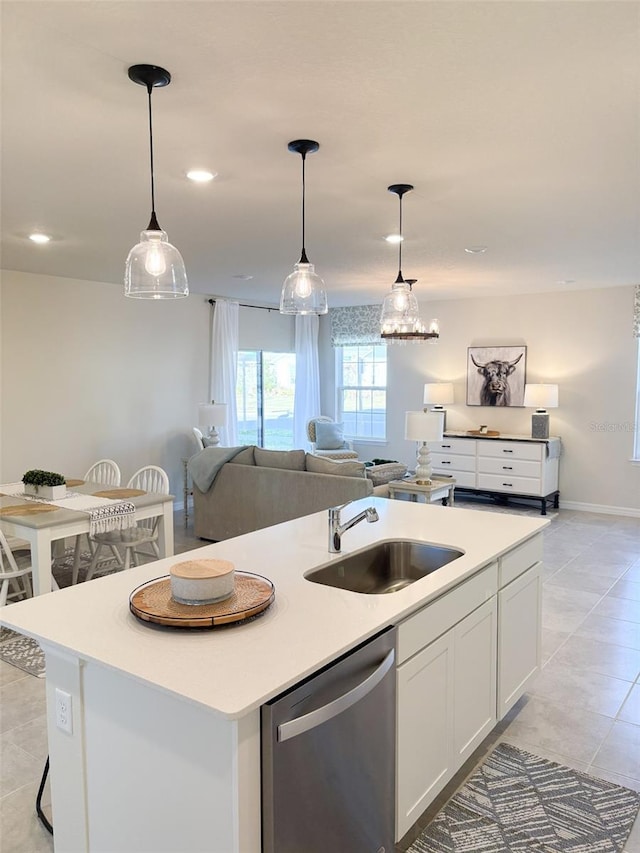 kitchen with stainless steel dishwasher, sink, white cabinetry, hanging light fixtures, and an island with sink