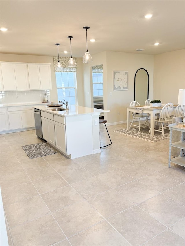 kitchen with pendant lighting, stainless steel dishwasher, decorative backsplash, a kitchen island with sink, and white cabinets