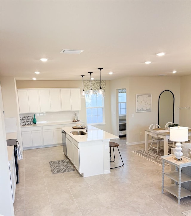 kitchen with white cabinets, decorative light fixtures, stainless steel appliances, sink, and a center island with sink