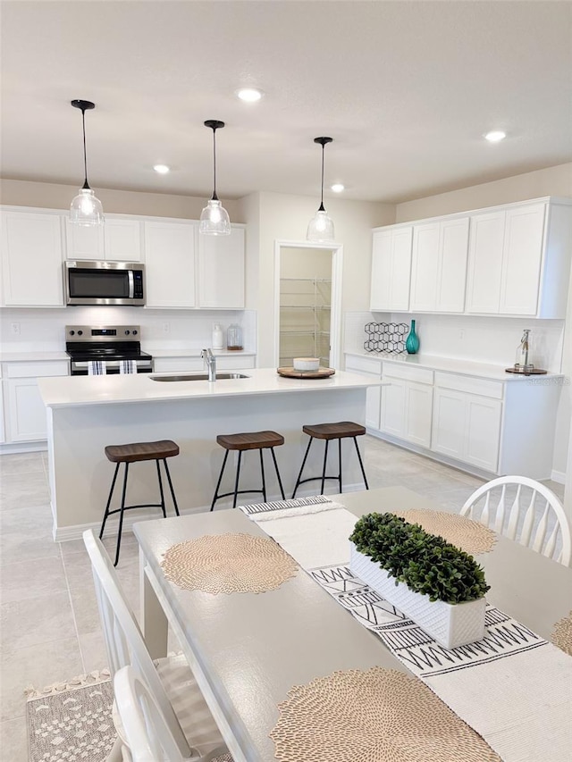 kitchen with stainless steel appliances, sink, white cabinetry, and decorative light fixtures