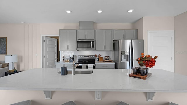 kitchen featuring appliances with stainless steel finishes, backsplash, light stone countertops, and a breakfast bar area