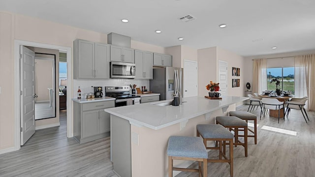 kitchen featuring stainless steel appliances, sink, a breakfast bar, a kitchen island with sink, and gray cabinetry