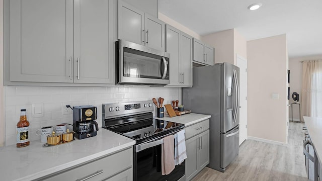 kitchen with light hardwood / wood-style floors, stainless steel appliances, gray cabinetry, light stone counters, and decorative backsplash