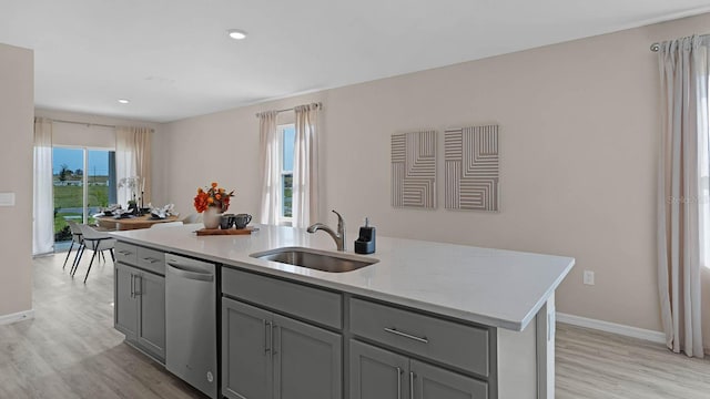 kitchen featuring sink, light wood-type flooring, an island with sink, stainless steel dishwasher, and a healthy amount of sunlight