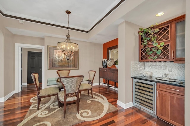 dining space with a notable chandelier, dark wood-type flooring, beverage cooler, ornamental molding, and indoor bar