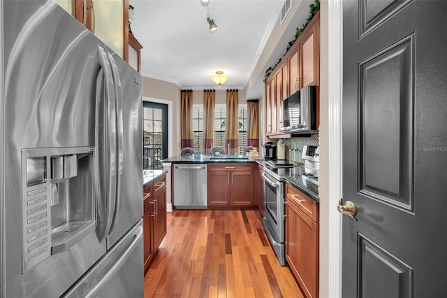 kitchen with a barn door, kitchen peninsula, crown molding, light wood-type flooring, and appliances with stainless steel finishes