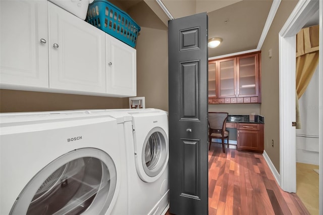 washroom featuring dark wood-type flooring, cabinets, ornamental molding, and washing machine and clothes dryer