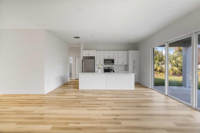 kitchen with appliances with stainless steel finishes, light hardwood / wood-style flooring, white cabinets, and a kitchen island with sink