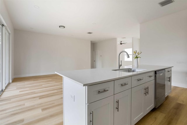 kitchen featuring stainless steel dishwasher, a kitchen island with sink, light hardwood / wood-style floors, and sink