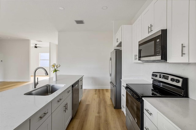 kitchen featuring appliances with stainless steel finishes, light hardwood / wood-style floors, ceiling fan, white cabinets, and sink