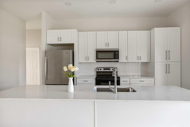 kitchen with appliances with stainless steel finishes, white cabinets, sink, and light stone countertops