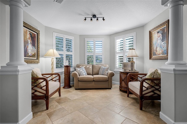 living area with rail lighting, a textured ceiling, and ornate columns