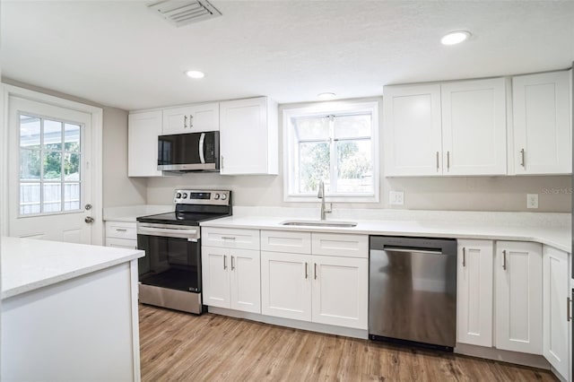 kitchen featuring stainless steel appliances, white cabinetry, sink, and light hardwood / wood-style floors