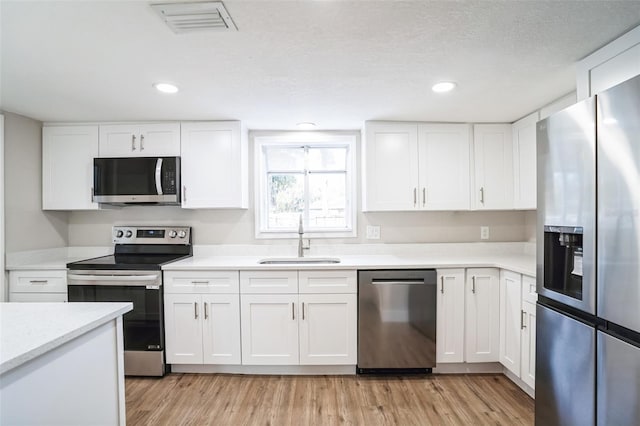 kitchen with stainless steel appliances, light wood-type flooring, white cabinetry, and sink