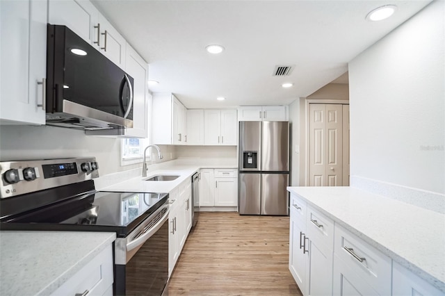 kitchen with stainless steel appliances, light wood-type flooring, light stone countertops, sink, and white cabinetry