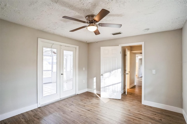 empty room with ceiling fan, french doors, a textured ceiling, and wood-type flooring