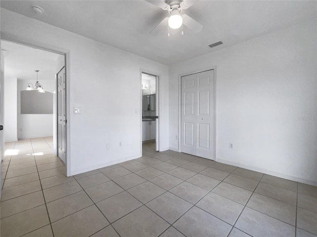 unfurnished bedroom featuring ceiling fan with notable chandelier, light tile patterned flooring, a closet, and connected bathroom