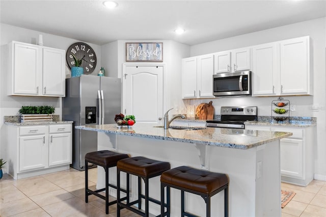 kitchen with appliances with stainless steel finishes, sink, white cabinets, light tile patterned floors, and a center island with sink