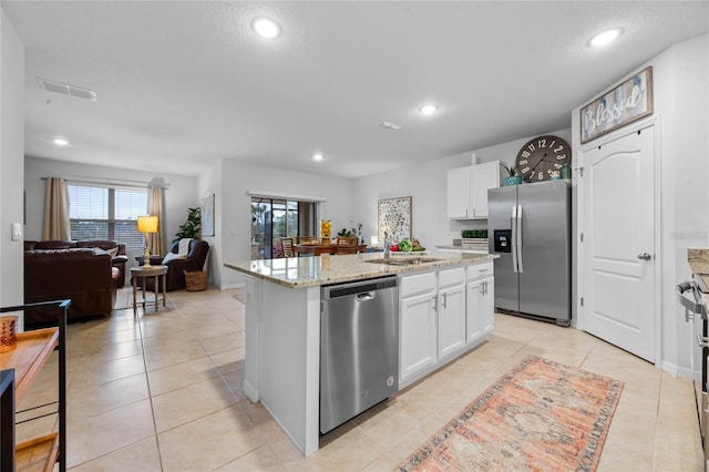 kitchen with white cabinetry, appliances with stainless steel finishes, a kitchen island with sink, and light stone counters