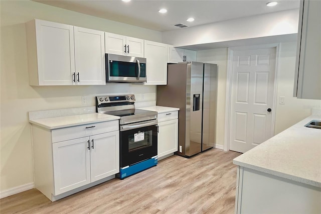 kitchen with stainless steel appliances, white cabinetry, and light wood-type flooring