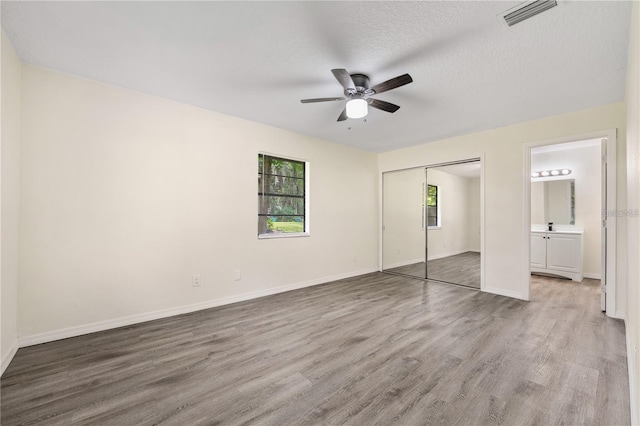 unfurnished bedroom with ensuite bathroom, a textured ceiling, ceiling fan, and hardwood / wood-style flooring