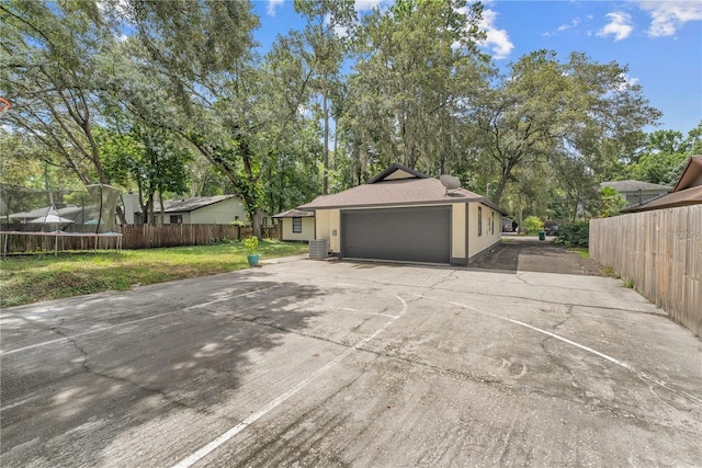 view of property exterior featuring central AC unit, a yard, a garage, and a trampoline