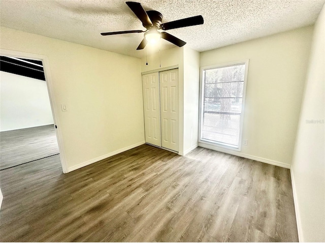 unfurnished bedroom featuring a textured ceiling, wood finished floors, a ceiling fan, baseboards, and a closet