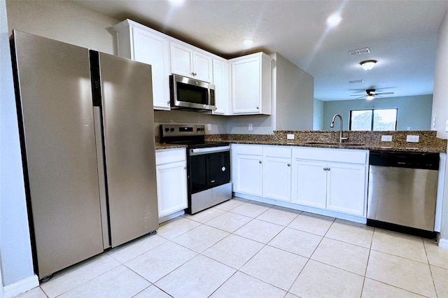 kitchen featuring appliances with stainless steel finishes, sink, white cabinets, dark stone counters, and light tile patterned floors