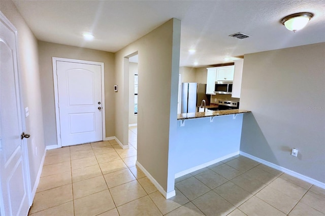 kitchen with white cabinetry, dark stone counters, light tile patterned floors, kitchen peninsula, and stainless steel appliances