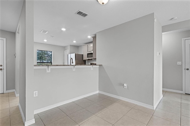 kitchen with appliances with stainless steel finishes, a breakfast bar, white cabinets, kitchen peninsula, and light stone countertops