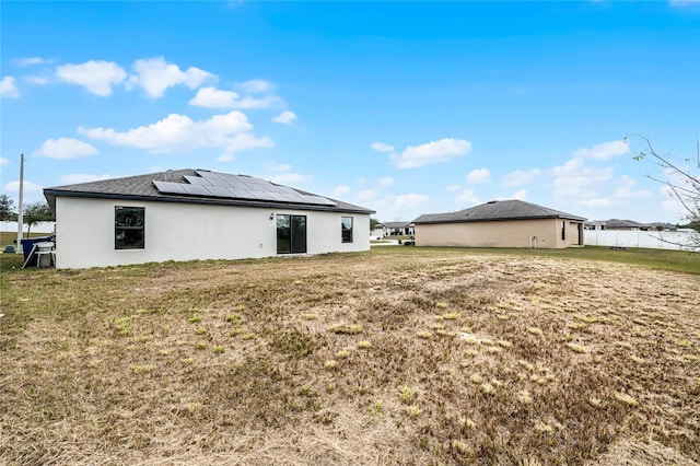 rear view of house featuring a yard and solar panels