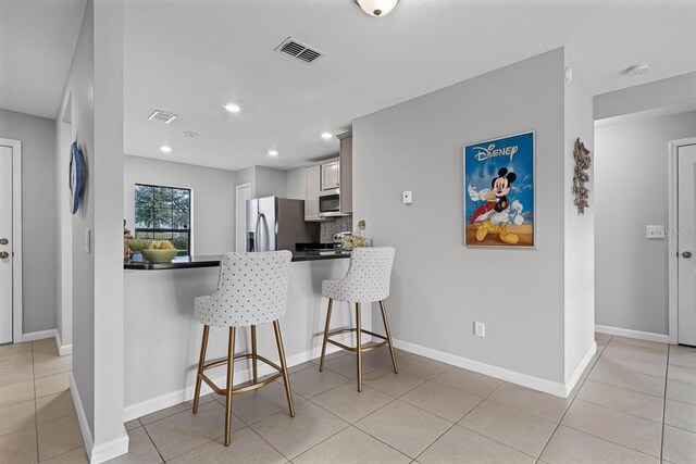 1952 Piedmont Ct, Mascotte, FL 34753 - kitchen with appliances with stainless steel finishes, a breakfast bar area, a peninsula, light tile patterned floors, and backsplash