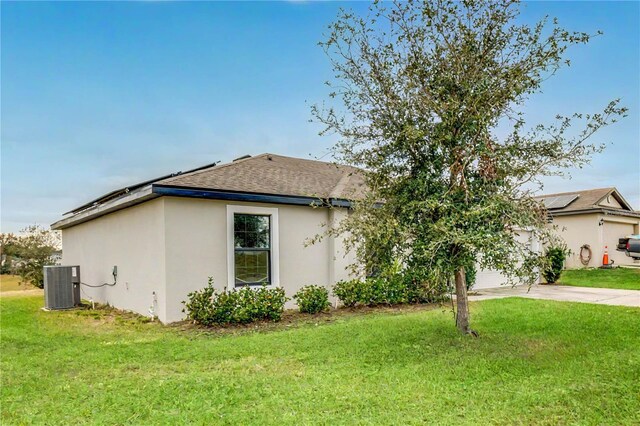 1952 Piedmont Ct, Mascotte, FL 34753 - view of property exterior featuring central air condition unit, stucco siding, roof with shingles, concrete driveway, and a lawn