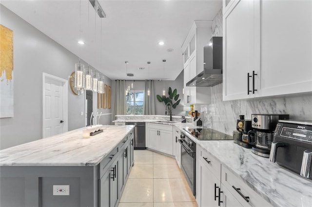 kitchen with decorative light fixtures, white cabinets, light stone counters, wall chimney exhaust hood, and a kitchen island