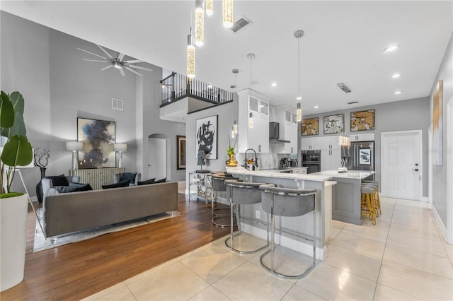 kitchen featuring decorative light fixtures, white cabinets, wall chimney exhaust hood, light tile patterned floors, and a breakfast bar area